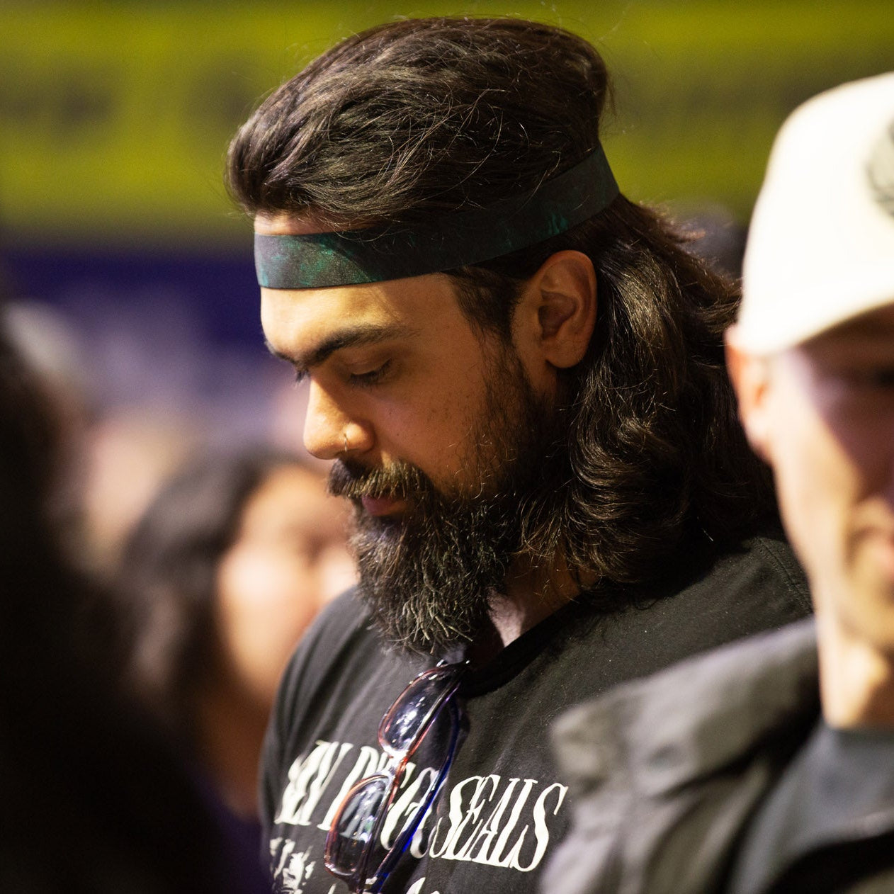 Man with long hair and beard wearing a headband and black t-shirt in a crowd.