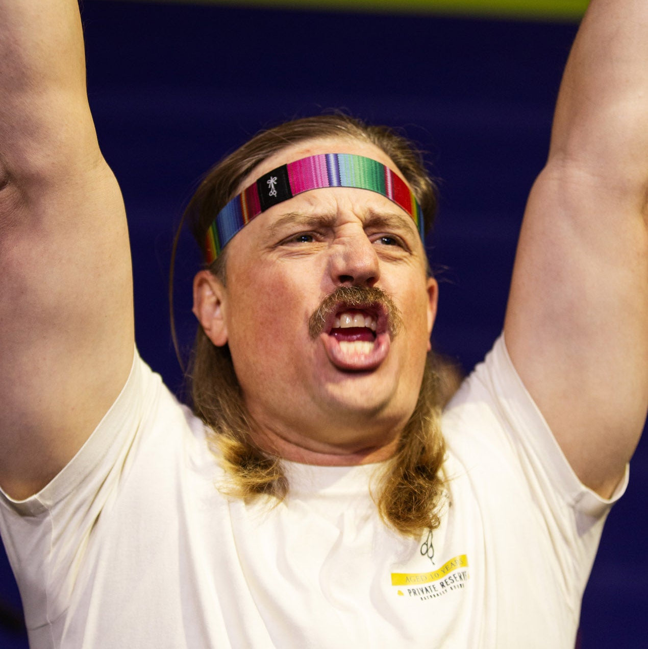 Man with a mustache and colorful headband lifting weights with a blurred background